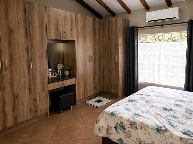 A well-maintained bedroom featuring extensive built-in wooden cabinetry with an integrated vanity, exposed timber ceiling beams, and split-system air conditioning.