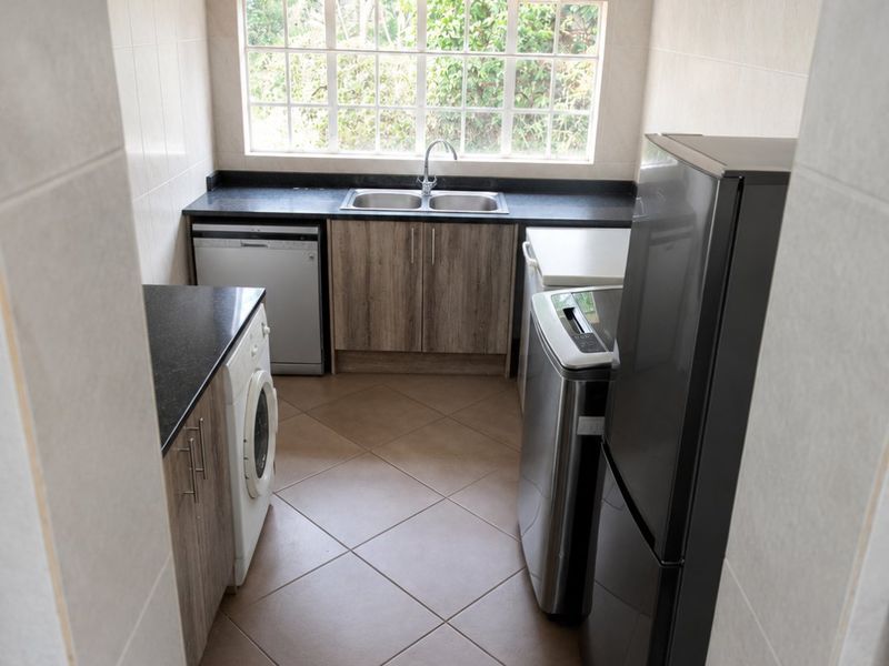 A functional laundry room featuring tiled walls and flooring, granite countertops, and a double basin sink with built-in cabinetry.