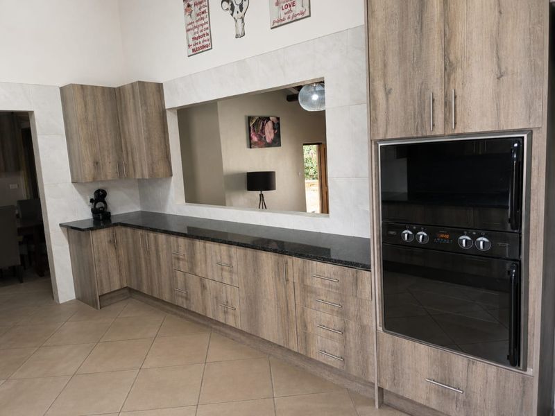 Modern kitchen featuring wood-look laminate cabinetry, dark granite countertops, a built-in oven, and a convenient pass-through window overlooking the adjacent living area.