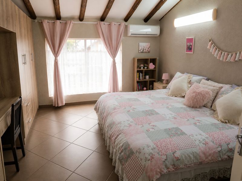 A well-maintained bedroom featuring exposed timber ceiling beams, tiled flooring, a built-in wardrobe, and a wall-mounted split-system air conditioner.