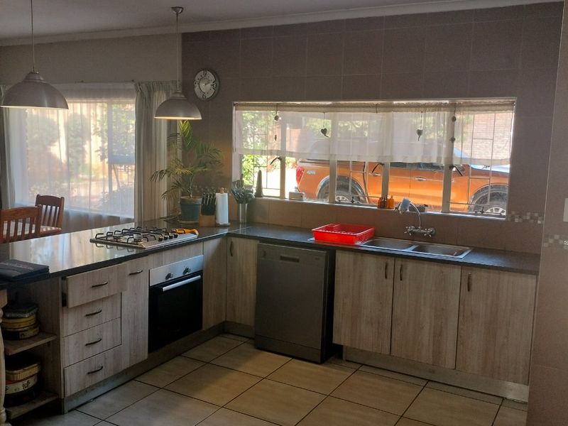 Functional kitchen featuring laminate cabinetry, built-in oven, gas hob, double sink, and tiled flooring with ample natural light.