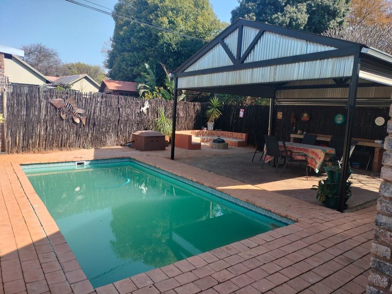 Outdoor entertainment area featuring a swimming pool, brick paved surround, and a covered patio structure with built-in seating.