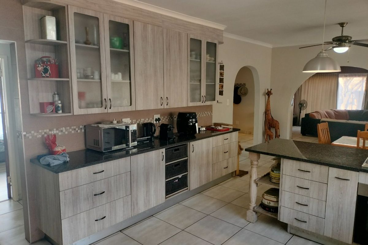 A functional kitchen featuring light wood-grain cabinetry, dark granite countertops, tiled flooring, and an open-plan layout connecting to the adjacent living area.