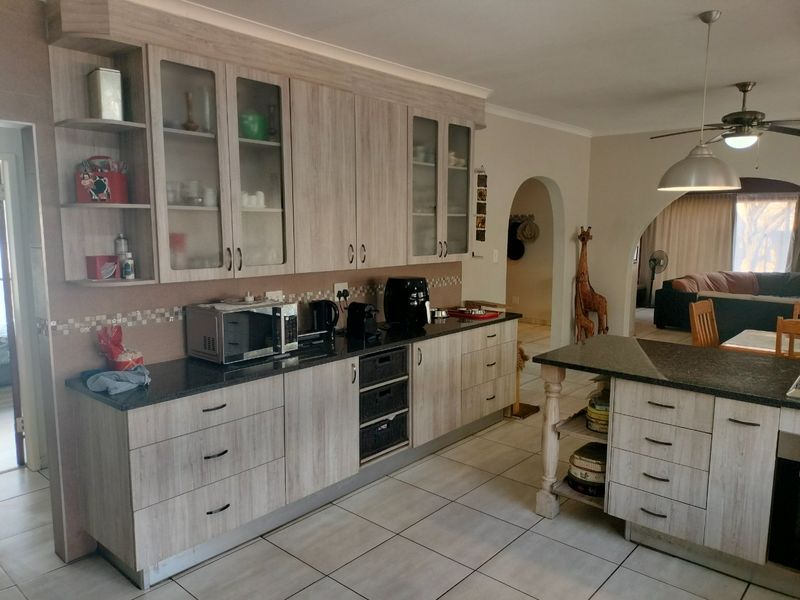 A functional kitchen featuring light wood-grain cabinetry, dark granite countertops, tiled flooring, and an open-plan layout connecting to the adjacent living area.