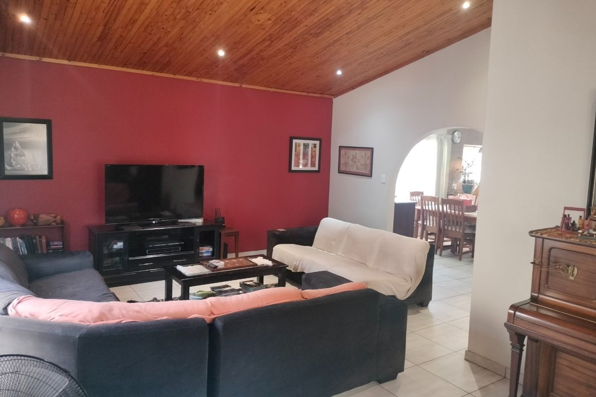 Spacious living room featuring a high timber raked ceiling with recessed downlights, tiled flooring, and an arched transition to the adjacent dining area.