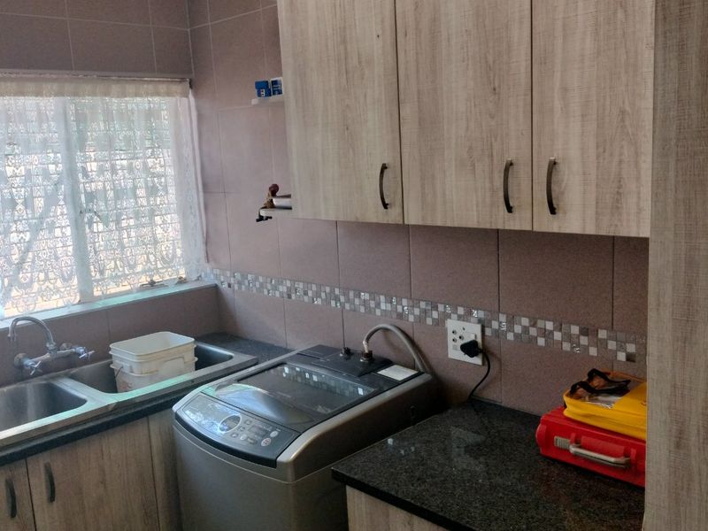 Functional laundry room featuring built-in wood-look cabinetry, granite countertops, and a double stainless steel sink with tiled splashback.