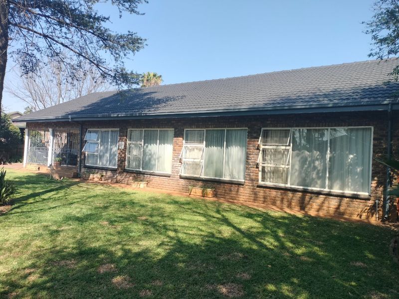 A view of the rear exterior of the house featuring a face brick facade, tiled roof, and large windows overlooking a lawn.