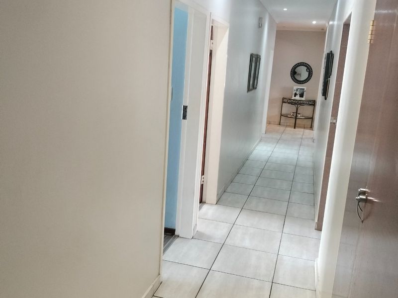 A clean and well-lit hallway featuring neutral ceramic floor tiles and recessed downlighting, providing access to multiple rooms.