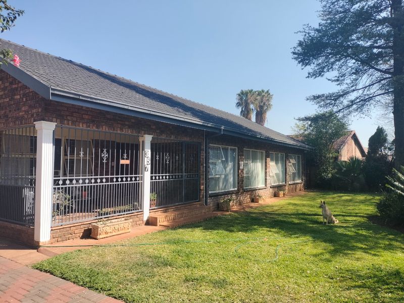 A front view of a face brick house featuring a covered patio with security gates, a tiled roof, and a well-maintained lawn.