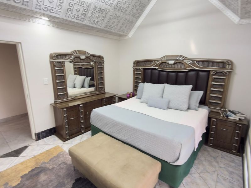 A spacious bedroom featuring unique decorative ceiling panels, tiled flooring, and recessed lighting, providing a comfortable and well-maintained sleeping area.