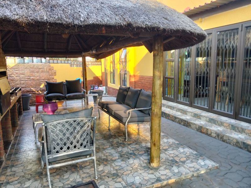 Covered outdoor patio area featuring a traditional thatched roof, built-in braai, and stone-tiled flooring, providing a functional space for outdoor entertaining.