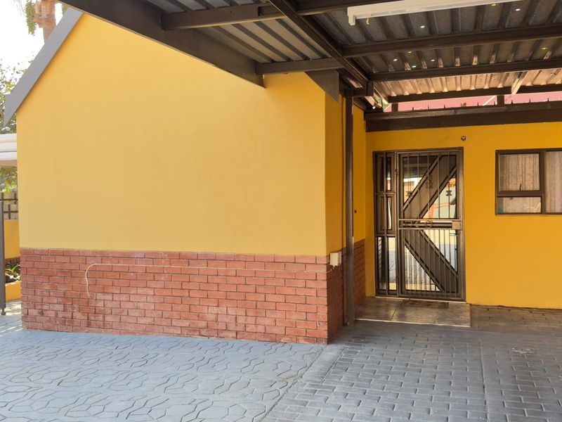 Front exterior view featuring a covered carport, paved driveway, and a secure entrance with a metal security gate.