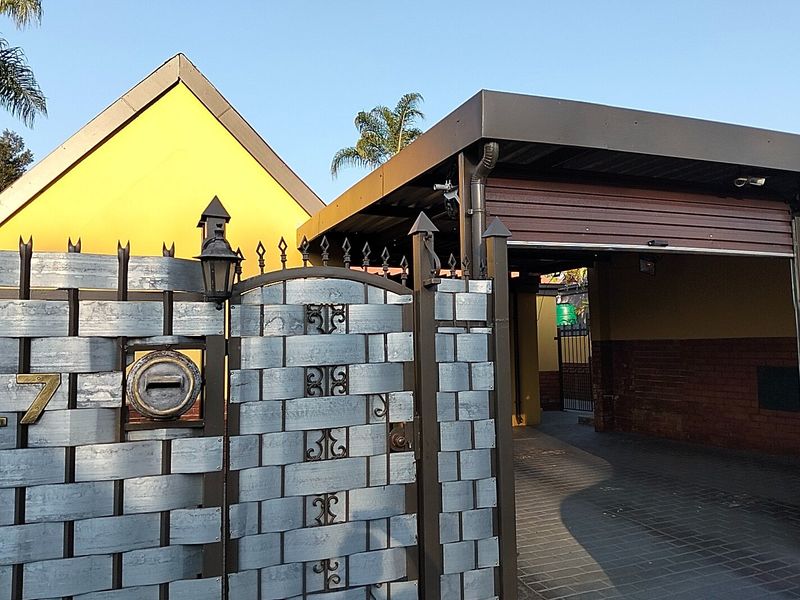 Front entrance view featuring a decorative metal security gate, paved driveway, and a covered carport area.