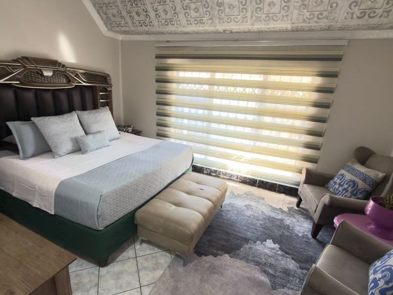 A well-maintained bedroom featuring patterned ceiling detailing, tiled flooring, and modern dual-layer roller blinds for adjustable natural light.