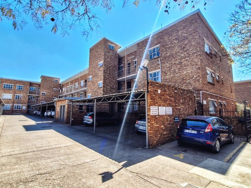 Exterior view of the apartment complex featuring a face brick facade and dedicated covered parking bays for residents.