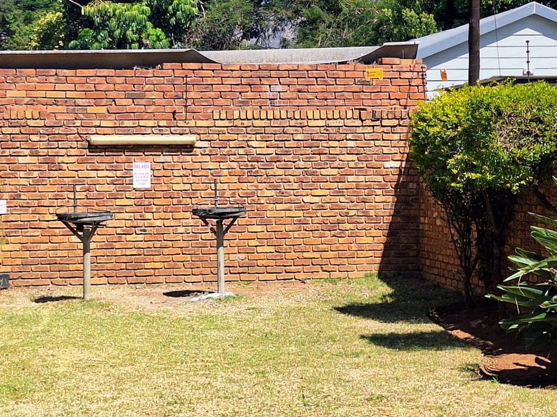 A rear outdoor area featuring a brick boundary wall and two built-in braai stands set within a grassed garden space.