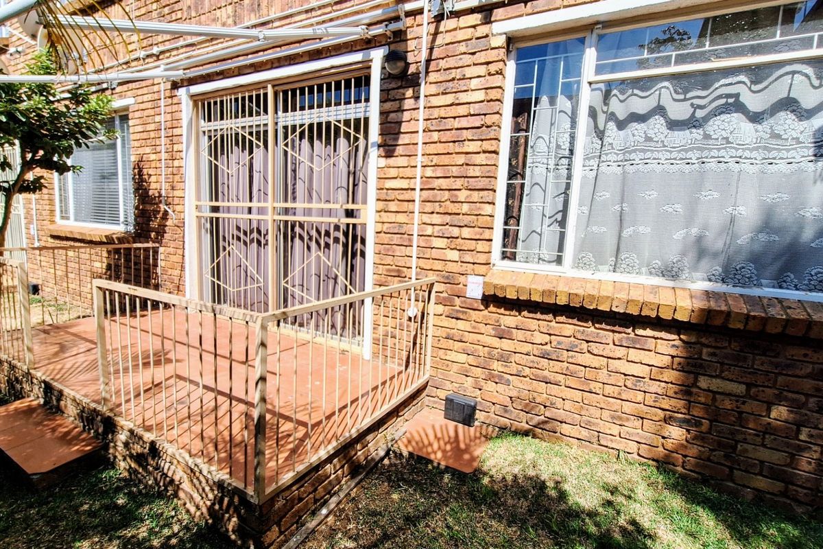 Rear exterior view of the apartment featuring a brick facade, a small tiled patio with metal railings, and security gates on the sliding door.