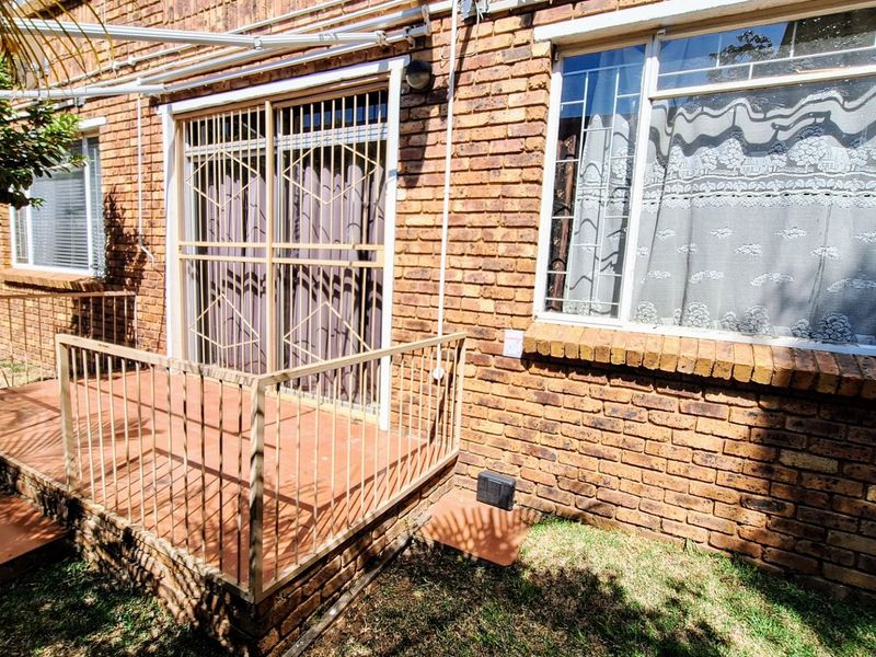 Rear exterior view of the apartment featuring a brick facade, a small tiled patio with metal railings, and security gates on the sliding door.