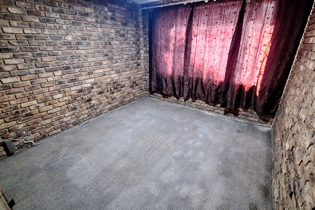 An empty bedroom featuring exposed brick walls and carpeted flooring, offering a blank canvas for renovation or interior design updates.