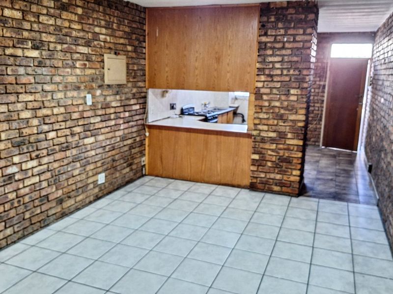 Open-plan living area featuring exposed brick walls, tiled flooring, and a pass-through kitchen window with built-in cabinetry.