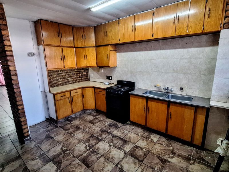 A functional kitchen featuring wooden cabinetry, a double basin sink, tiled backsplash, and a freestanding stove, set against an exposed brick wall.