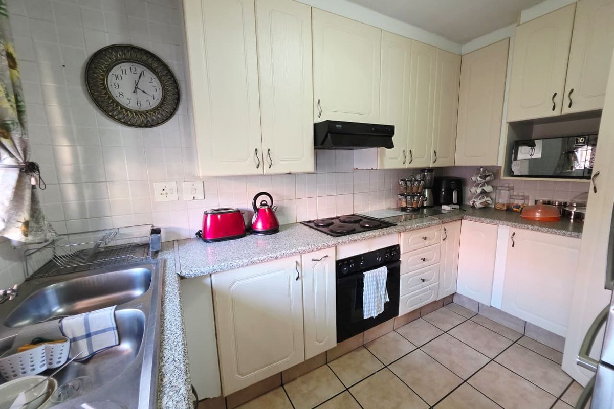 Functional kitchen featuring ample built-in cabinetry, laminate countertops, a double stainless steel sink, and integrated cooking appliances with tiled flooring and backsplash.
