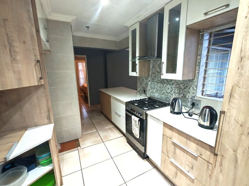 Modern kitchen featuring wood-grain and white cabinetry, stone countertops, a gas stove with extractor fan, and decorative tiled backsplash.