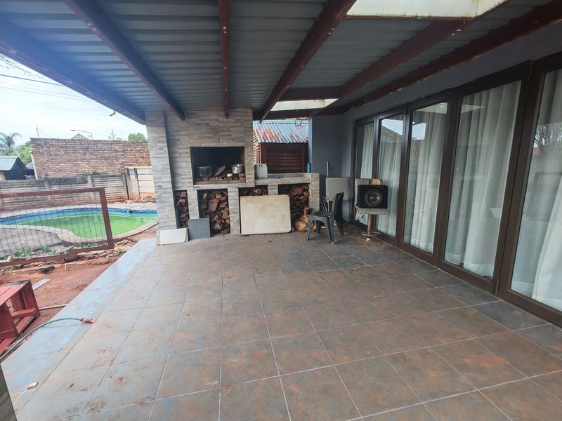 Covered outdoor patio featuring a built-in braai, tiled flooring, and direct access to the garden and pool area through large sliding glass doors.