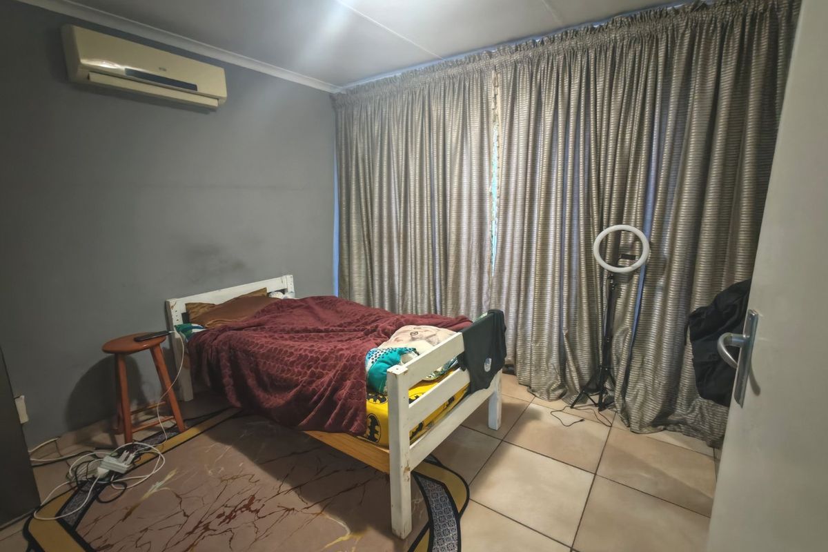 A functional bedroom featuring tiled flooring, a wall-mounted air conditioning unit, and full-length window curtains.