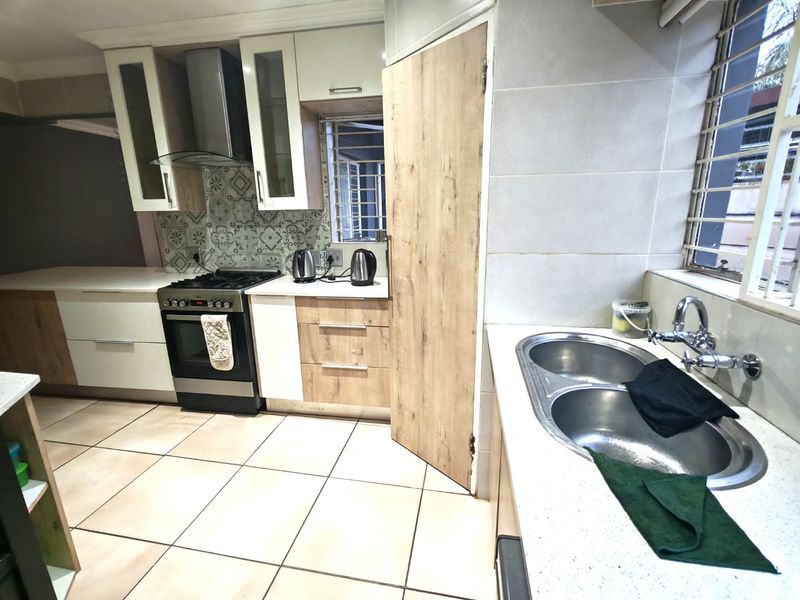 Modern kitchen featuring wood-look and white cabinetry, stainless steel double sink, gas stove with extractor fan, and tiled flooring.