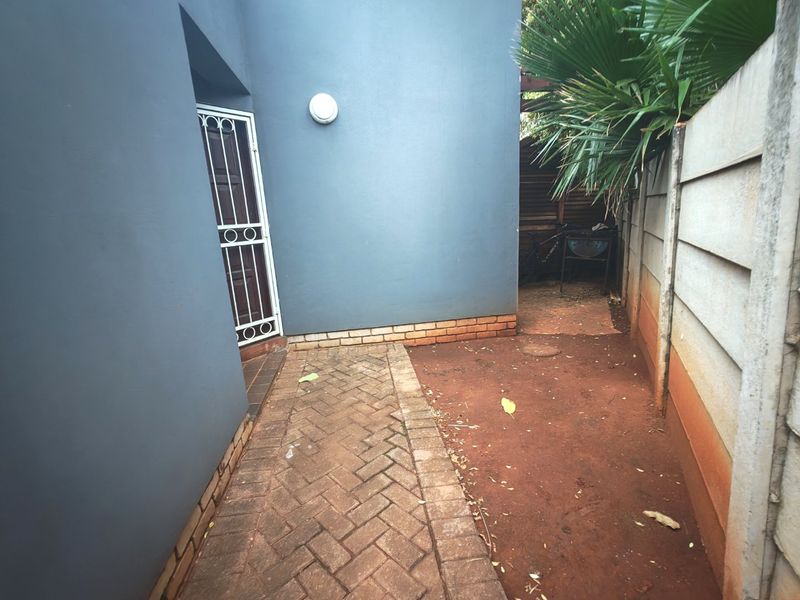 A side or rear exterior area featuring brick paving, a security gate, and a precast concrete boundary wall.