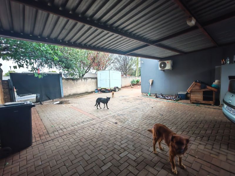 A covered outdoor patio area featuring paved flooring and a corrugated metal roof, providing a functional space for parking or outdoor activities.