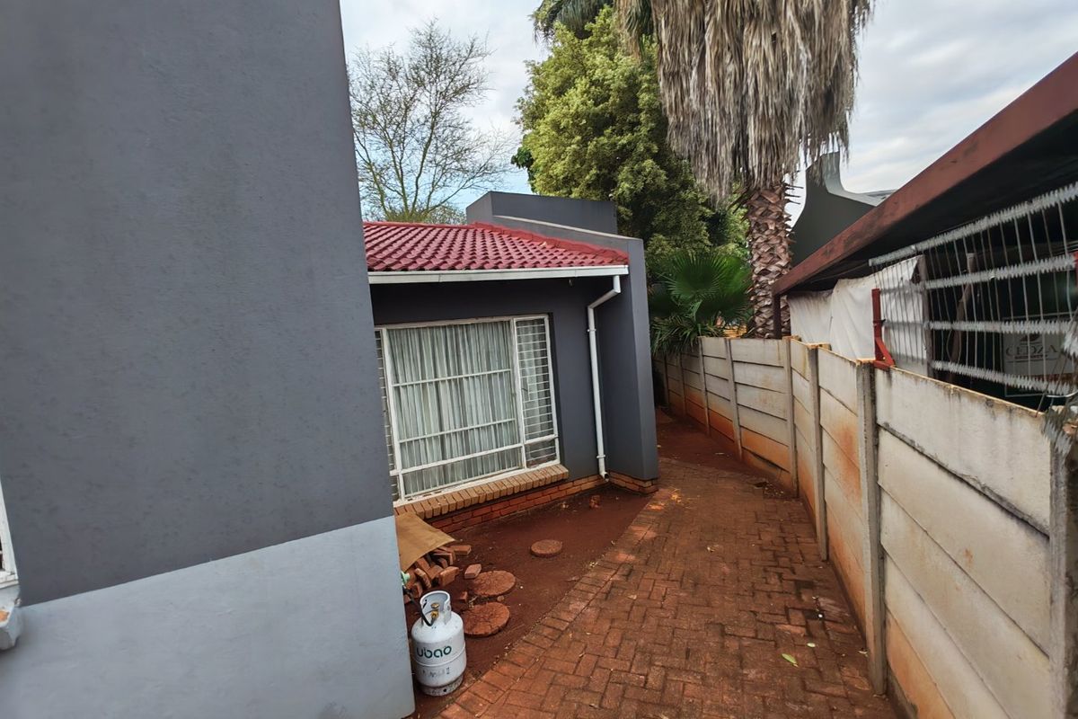 A side view of the property showing a paved walkway, precast concrete boundary wall, and exterior wall finishes with a tiled roof.