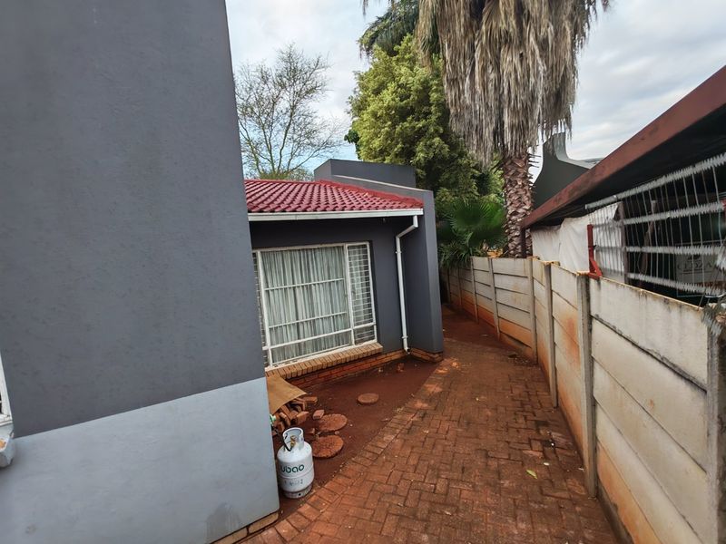 A side view of the property showing a paved walkway, precast concrete boundary wall, and exterior wall finishes with a tiled roof.