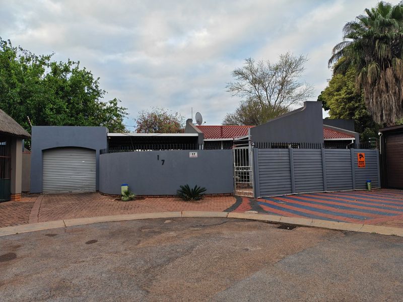 Front exterior view of the property featuring a paved driveway, enclosed perimeter wall with security spikes, and a single roller garage door.