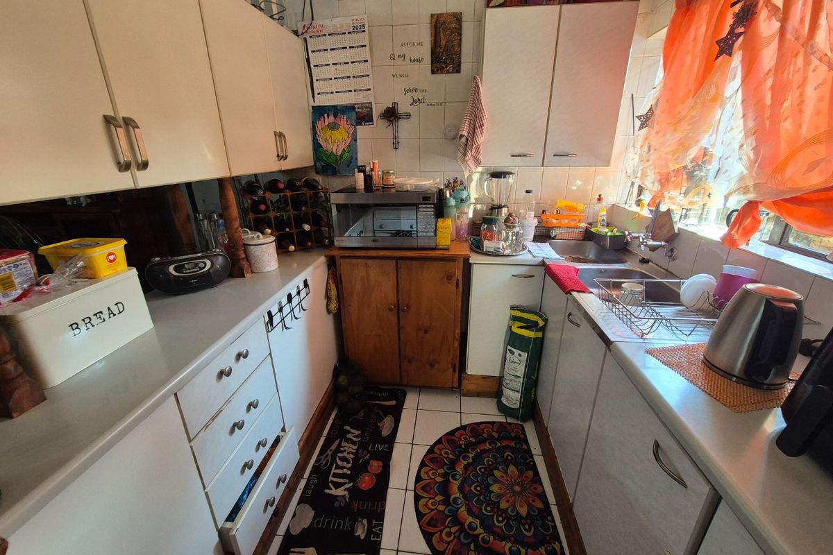 A compact kitchen featuring white cabinetry, laminate countertops, a stainless steel sink, and tiled finishes, offering a functional layout for daily meal preparation.
