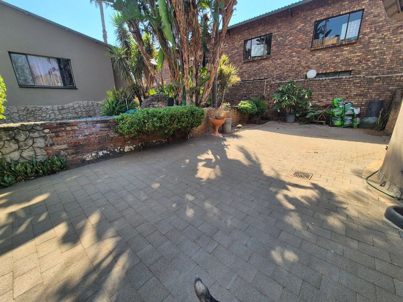 A paved rear courtyard area featuring a brick retaining wall, mature landscaping, and face brick exterior walls of the house.