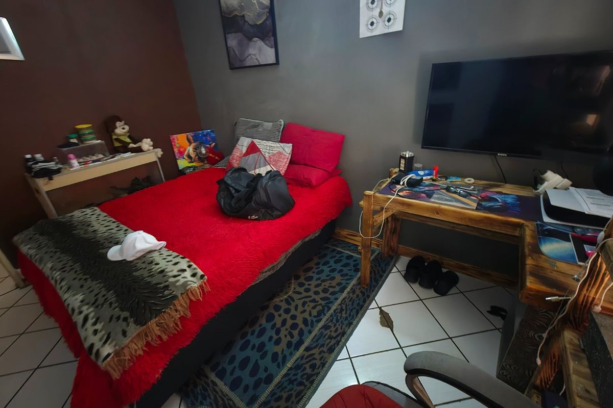 A bedroom featuring tiled flooring and painted walls, currently utilized as a combined sleeping and workspace area.