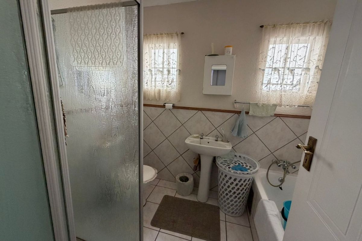 A functional bathroom featuring a pedestal basin, a bathtub, and a separate shower enclosure with tiled finishes.