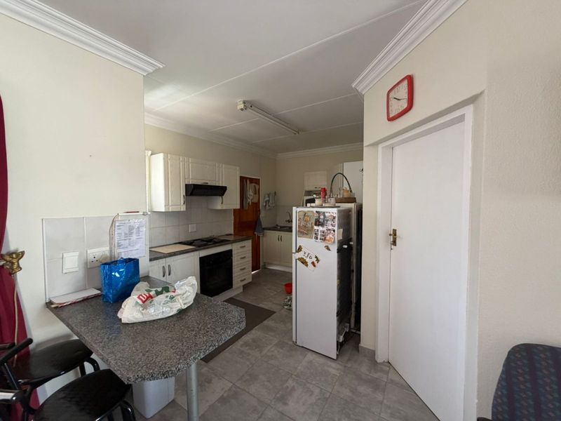 A functional kitchen featuring built-in cabinetry, a hob, oven, extractor fan, and a breakfast counter with tiled flooring and backsplash.