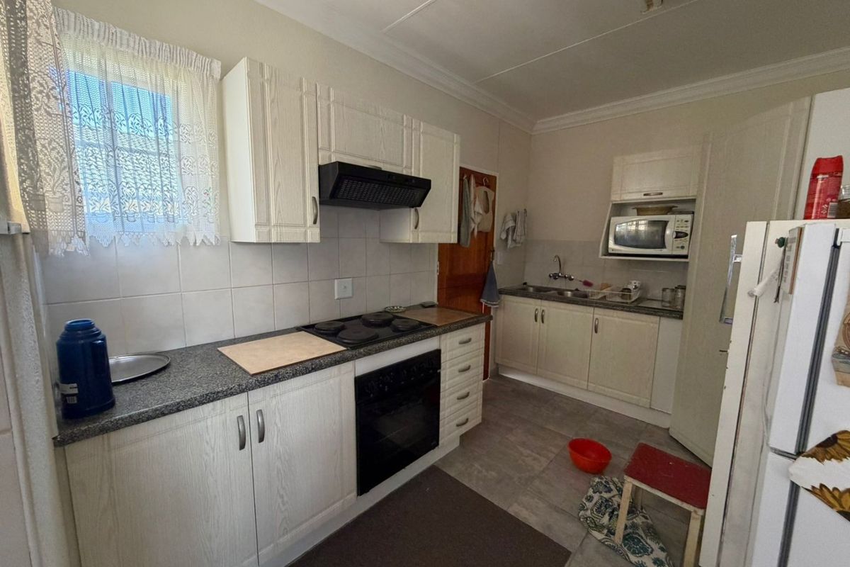 Functional kitchen featuring built-in cabinetry, granite countertops, electric hob, oven, extractor fan, and double sink with tiled backsplash and flooring.