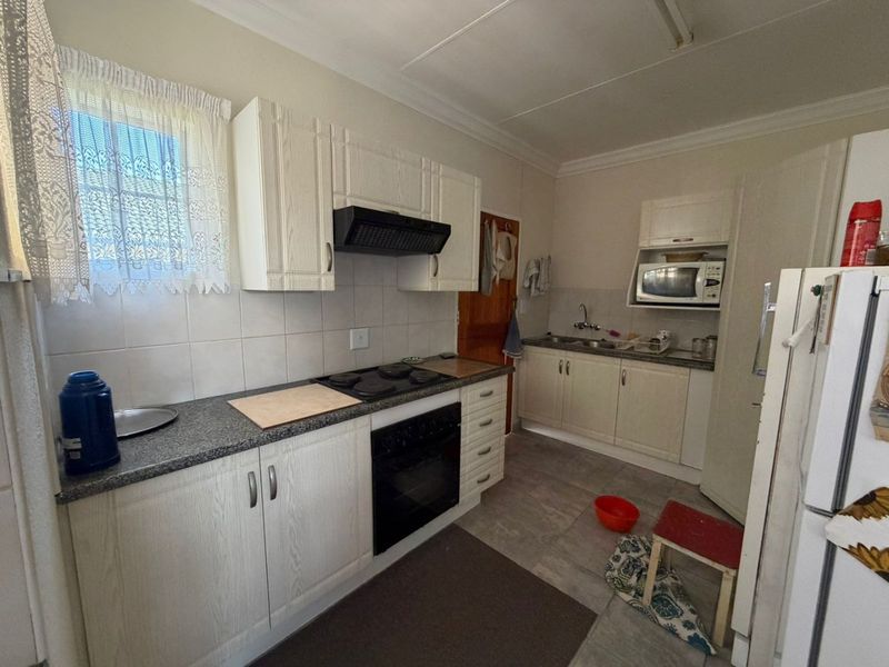 Functional kitchen featuring built-in cabinetry, granite countertops, electric hob, oven, extractor fan, and double sink with tiled backsplash and flooring.