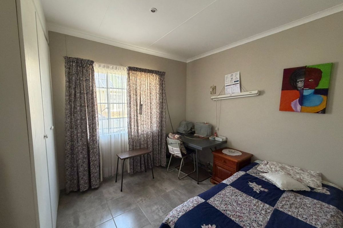 A functional bedroom featuring tiled flooring, built-in cupboards, and natural light through a window with curtains.