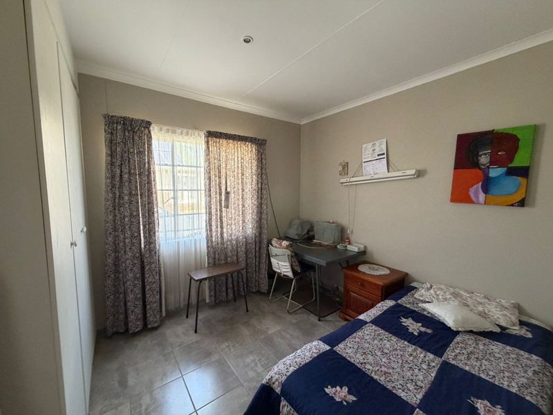 A functional bedroom featuring tiled flooring, built-in cupboards, and natural light through a window with curtains.