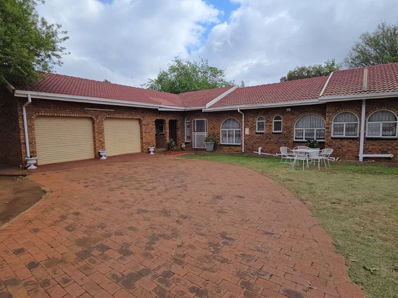 Front view of a single-story brick house featuring a double garage, paved driveway, and arched windows with security bars.