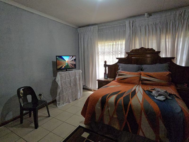 A bedroom featuring tiled flooring and window curtain tracks, requiring cosmetic updates to the wall finishes to improve the overall aesthetic.