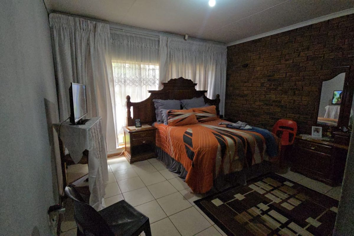 A bedroom featuring an exposed brick feature wall, tiled flooring, and a sliding glass door providing natural light.