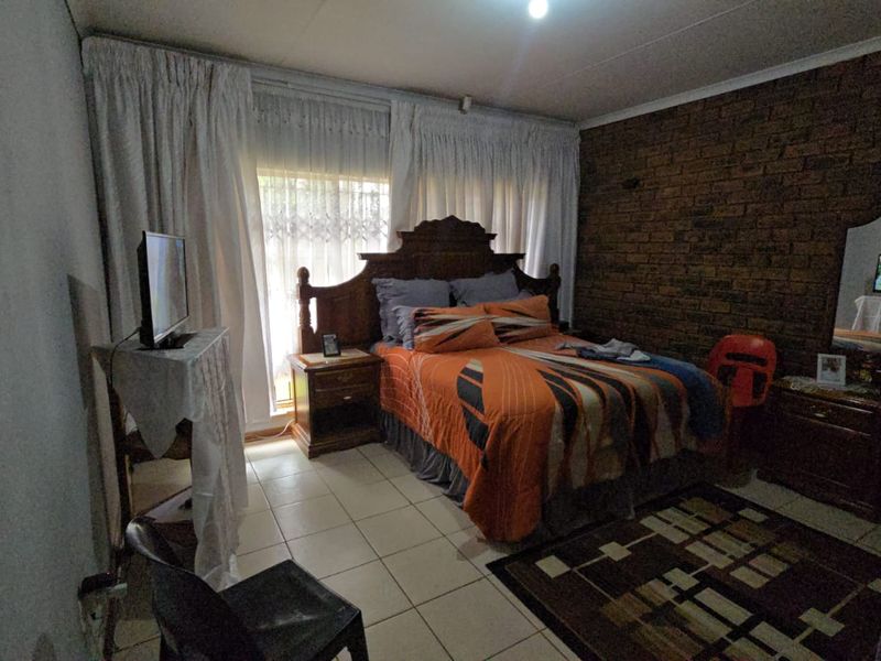 A bedroom featuring an exposed brick feature wall, tiled flooring, and a sliding glass door providing natural light.