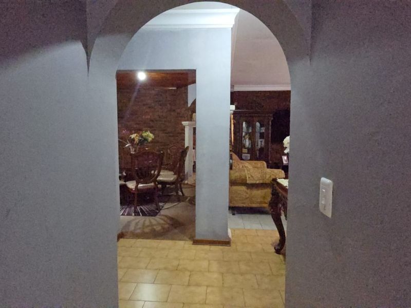 A view through an arched doorway into a living area featuring tiled flooring and crown molding.