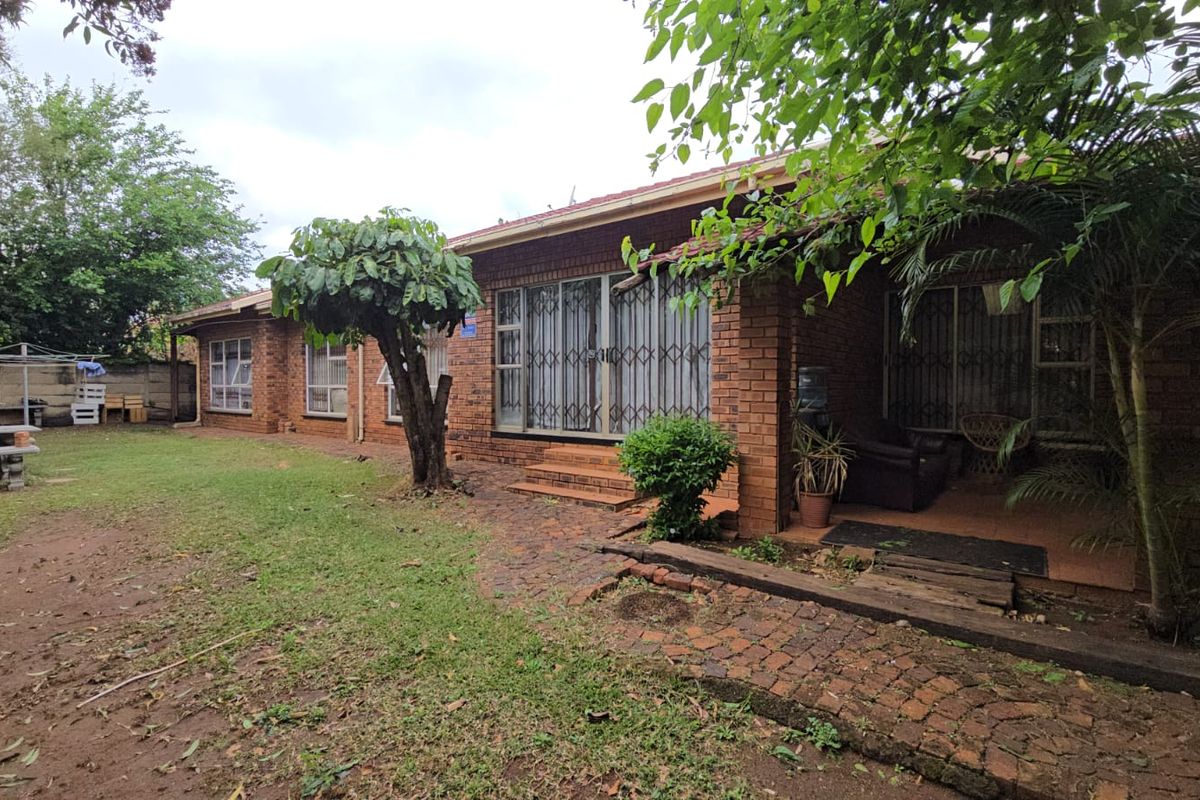 Rear view of a brick house featuring a covered patio, security gates, and a spacious garden area with a paved walkway.
